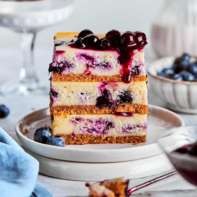 Three blueberry cheesecake bars are stacked on a plate.