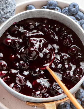 a spoon in a pan of fresh blueberry sauce, plus fresh blueberries