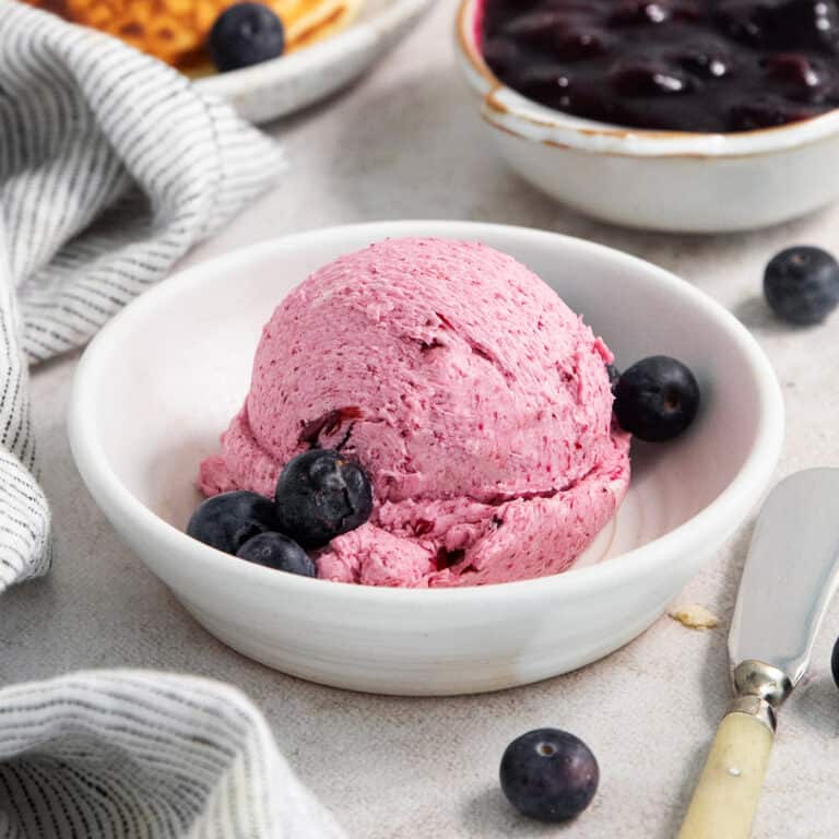 A white bowl holds a big scoop of blueberry butter with fresh bluberries around it.