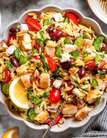 a serving spoon in a white bowl full of orzo salad