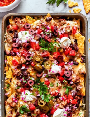 overhead photo of a rimmed pan full of baked cheesy nachos loaded with meat and vegetables