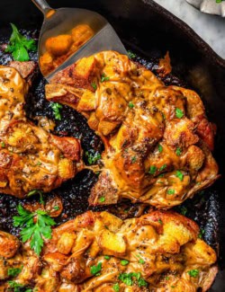 a cast iron skillet with juicy baked pork chops covered in stuffing and gravy